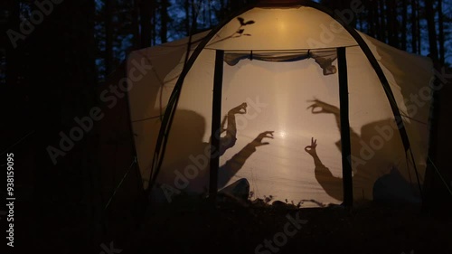 Children making shadow puppets in a camping tent at night