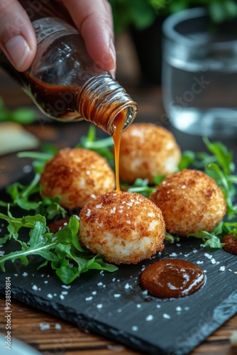 Hand drizzling sauce over crispy fried food on a slate plate