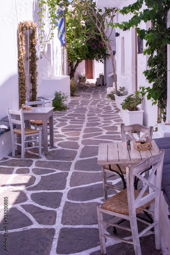 Calle típica cíclada blanca y estrecha, con mesas y sillas, en la localidad de Naoussa, isla de Paros photo