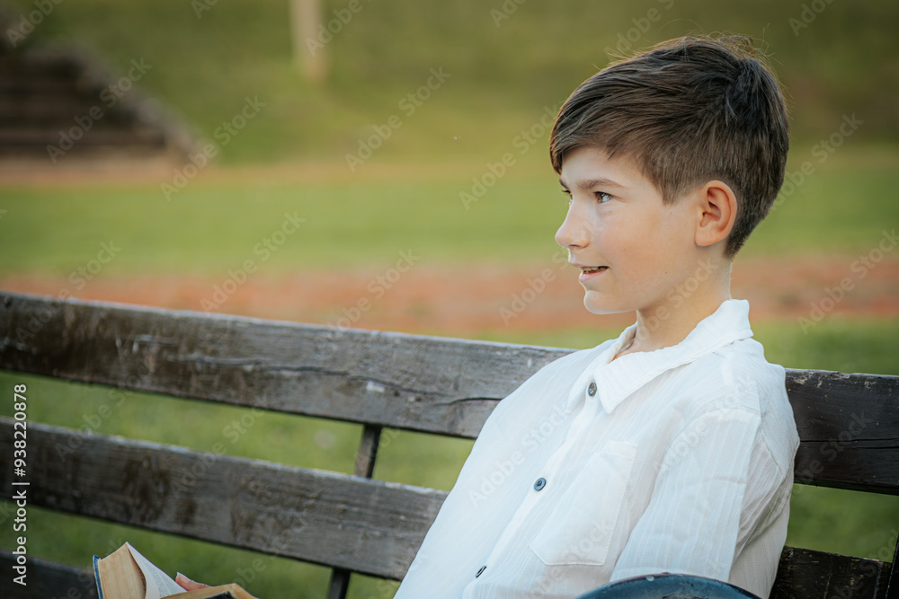 A young boy sits on a park bench, looking intently at the camera with a serious expression. The green, blurred background creates a calm outdoor setting, contrasting with his focused demeanor. A young boy sits on a park bench, looking intently at the camera with a serious expression. The green, blurred background creates a calm outdoor setting, contrasting with his focused demeanor.