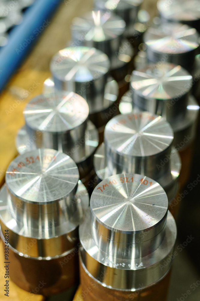 Close-up of freshly machined metallic parts arranged in a line on factory workbench catching light from nearby sources. Parts display clean surfaces with reflective finishes Close-up of freshly machined metallic parts arranged in a line on factory workbench catching light from nearby sources. Parts display clean surfaces with reflective finishes