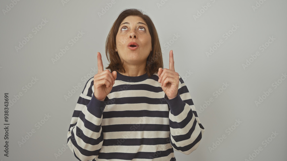 A middle-aged hispanic woman in a striped sweater gestures upward against a white background, expressing surprise or curiosity. A middle-aged hispanic woman in a striped sweater gestures upward against a white background, expressing surprise or curiosity.