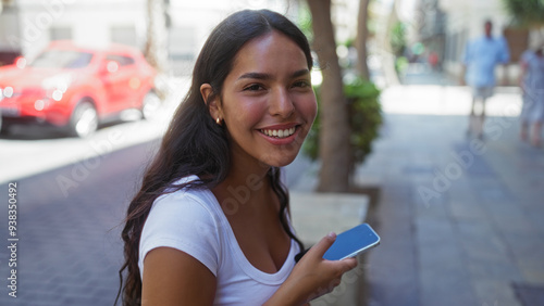 Foto Young woman holding a phone and smiling on a city street, exuding happiness and vibrancy in an urban setting