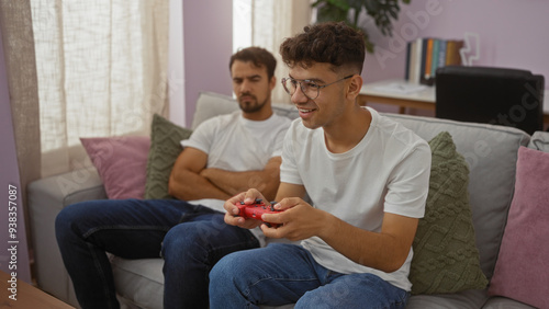 Father and son in a cozy living room at home with the son playing video games while the father looks on, capturing a moment of family bond and modern-day leisure