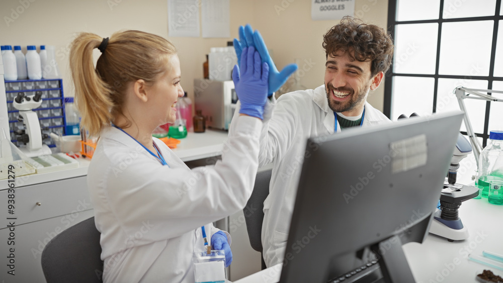 Obraz premium A man and woman in lab coats high-five in a bright laboratory, embodying teamwork and success in a medical or scientific environment.