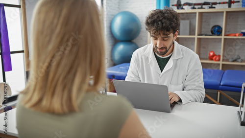 A woman patient consults with a male doctor in a modern clinic's interior, using a laptop.