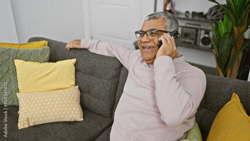 Fototapeta premium Smiling senior man using smartphone on couch in cozy living room