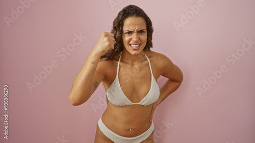 Angry young hispanic woman in bikini poses against isolated pink background