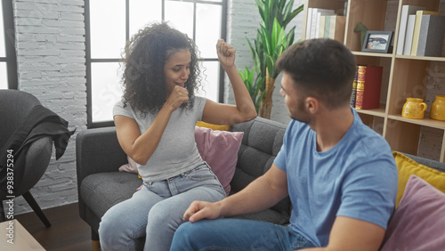 A happy couple engages in a playful arm wrestling match on a cozy sofa in a modern living room, epitomizing a joyful, loving relationship.