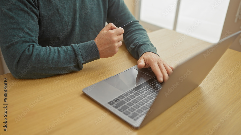 A young man with a beard working on a laptop at a wooden table indoors. A young man with a beard working on a laptop at a wooden table indoors.
