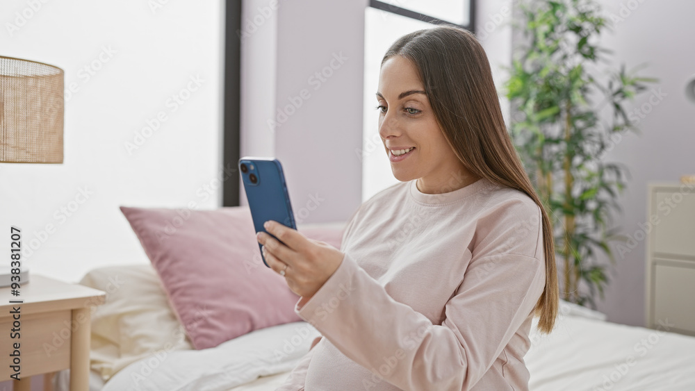 A smiling pregnant woman using a smartphone in a cozy bedroom setting, exuding warmth and tranquility. A smiling pregnant woman using a smartphone in a cozy bedroom setting, exuding warmth and tranquility.
