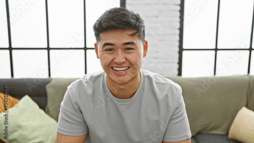 Smiling young asian man in a casual t-shirt posing indoors in a stylish apartment. photo