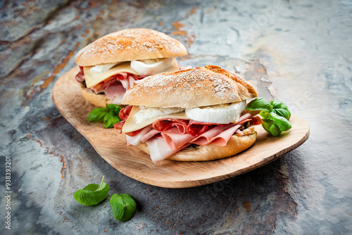 Traditional New Orleans muffaletta sandwiches with mortadella, salami and provolone cheese served in an Italian ciabatta bread as close-up on a wooden design cutting board photo