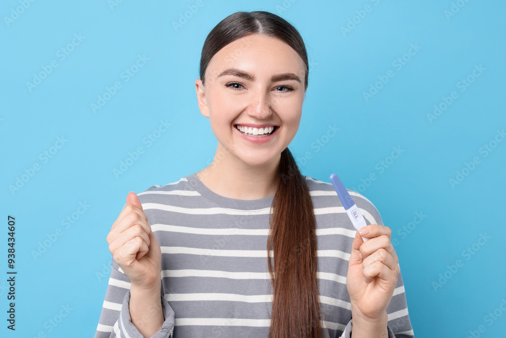 Happy woman holding pregnancy test on light blue background Happy woman holding pregnancy test on light blue background