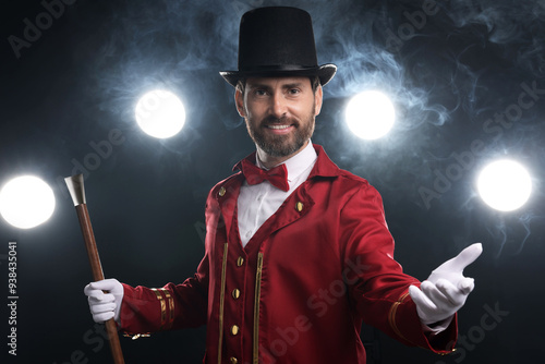 Portrait of showman in red costume, cane and hat on black background with spotlights and smoke