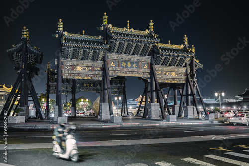 In the ancient city of Datong, Shanxi, the Yongtai Street Archway stands in the center of a roundabout, surrounded by busy traffic and a person passing by on an electric bike. photo