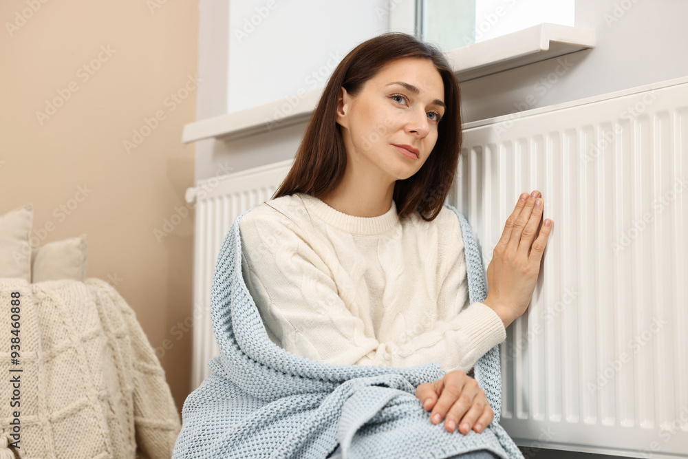 Woman with blanket warming near heating radiator at home Woman with blanket warming near heating radiator at home