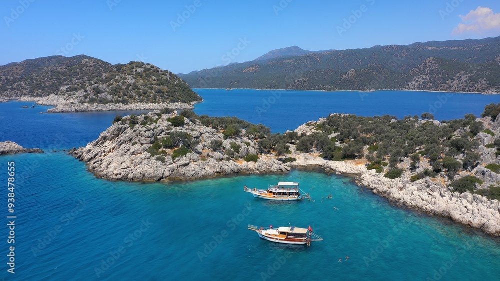 Crystal clear turquoise waters, rugged rocky shores, boats anchored near the coastline, and swimmers enjoying the serene environment. Aerial view of Aquarium Bay at Kekova, Turkey Crystal clear turquoise waters, rugged rocky shores, boats anchored near the coastline, and swimmers enjoying the serene environment. Aerial view of Aquarium Bay at Kekova, Turkey