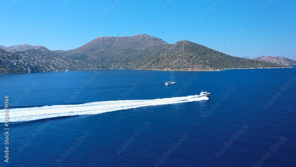 Fototapeta premium Coast guard boat heading full speed off the coast of Datça, leaving a long white trail of foam behind. Aerial a fast powerboat of Turkish Customs training and sailing in Mediterranean Sea. 