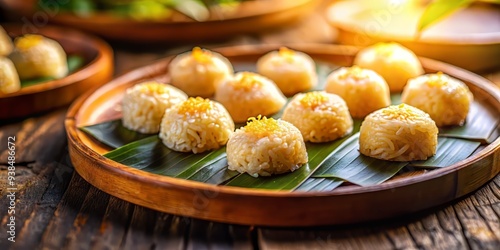 Golden hour captures Khanom Thien sticky rice cakes arranged in artistic pattern on intricately carved wooden platter with subtle blurred motion and shallow depth. photo