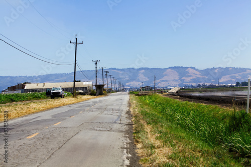 Rural Road With Agricultural Fields And Hills In Background