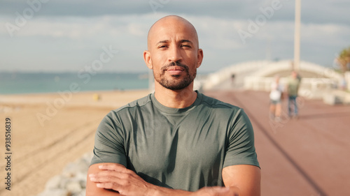 Portrait of confident male athlete against blured background of the sea and sky with arms crossed on his chests