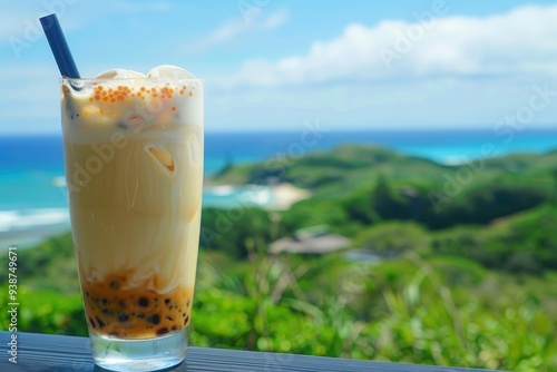 A refreshing glass of bubble tea on a table, overlooking a lush green landscape and clear blue ocean under a sunny sky.