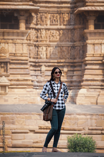 An Indian girl smiles and holds a camera, ready to capture photographs of the historic Khajuraho Hindu temple, showcasing excitement and cultural exploration.