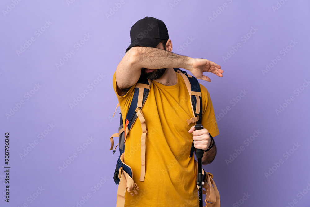 Caucasian handsome man with backpack and trekking poles over isolated background covering eyes by hands Caucasian handsome man with backpack and trekking poles over isolated background covering eyes by hands