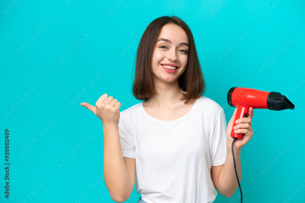 Young Ukrainian holding a hairdryer isolated on blue background pointing to the side to present a product Young Ukrainian holding a hairdryer isolated on blue background pointing to the side to present a product