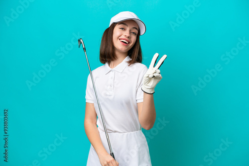 Young Ukrainian golfer player woman isolated on blue background smiling and showing victory sign photo