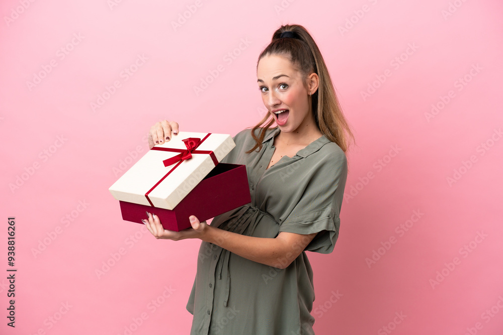 Young woman isolated on pink background pregnant and holding a gift with surprised expression Young woman isolated on pink background pregnant and holding a gift with surprised expression