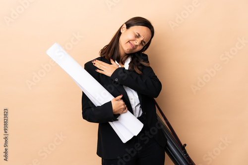 Young architect woman holding blueprints over isolated background suffering from pain in shoulder for having made an effort