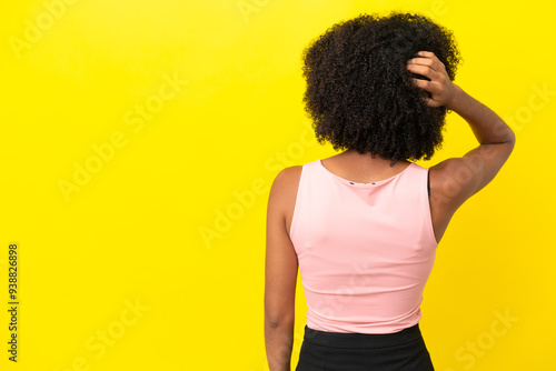 Young African American woman isolated on yellow background in back position and thinking