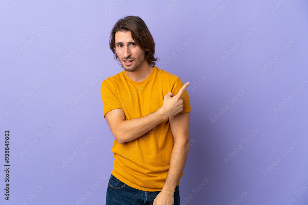 Young handsome man isolated on purple background surprised and pointing side Young handsome man isolated on purple background surprised and pointing side