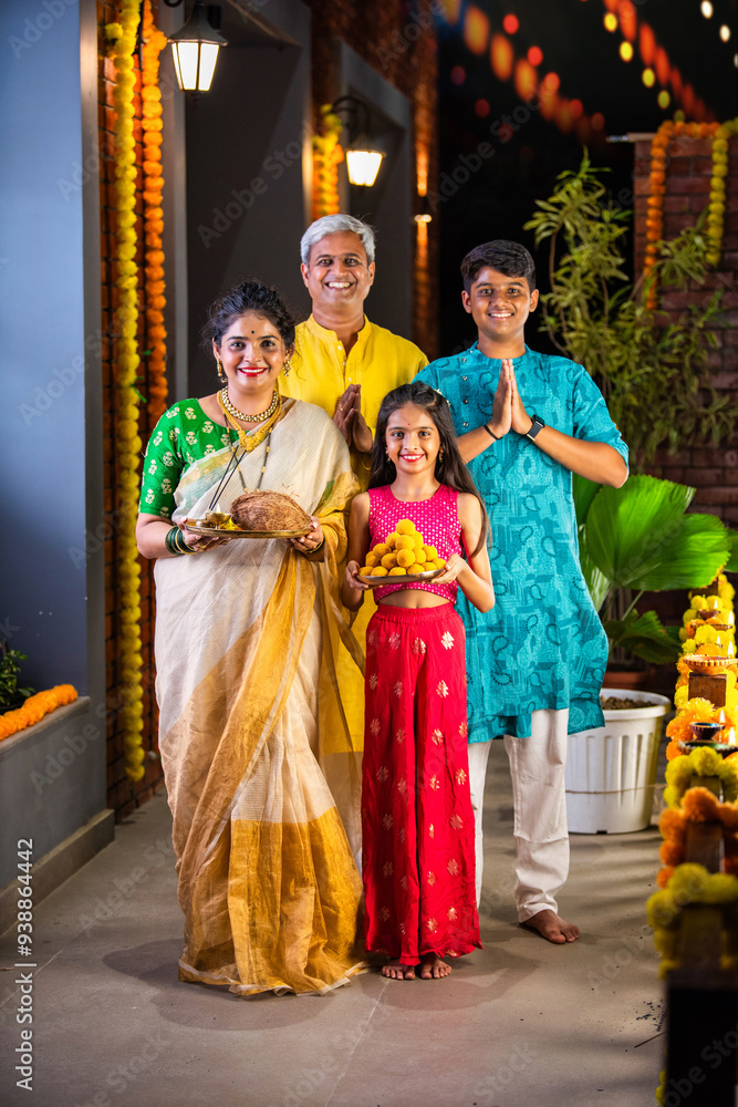 Obraz premium Indian parents with children celebrating Diwali on the balcony, holding Pooja thali and sweets.