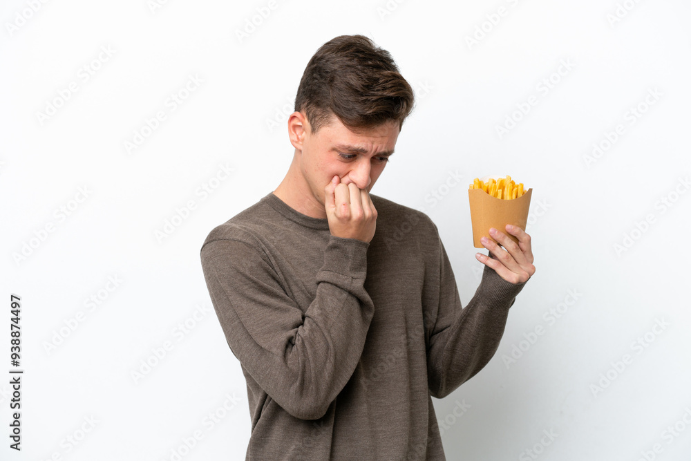 Young Brazilian man holding fried chips isolated on white background having doubts Young Brazilian man holding fried chips isolated on white background having doubts