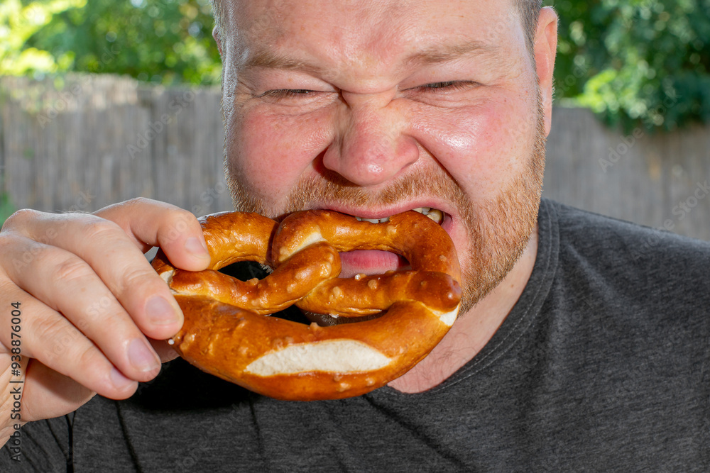 A Caucasian man enthusiastically bites into a large pretzel in celebration of Oktoberfest, symbolizing festive indulgence and tradition A Caucasian man enthusiastically bites into a large pretzel in celebration of Oktoberfest, symbolizing festive indulgence and tradition