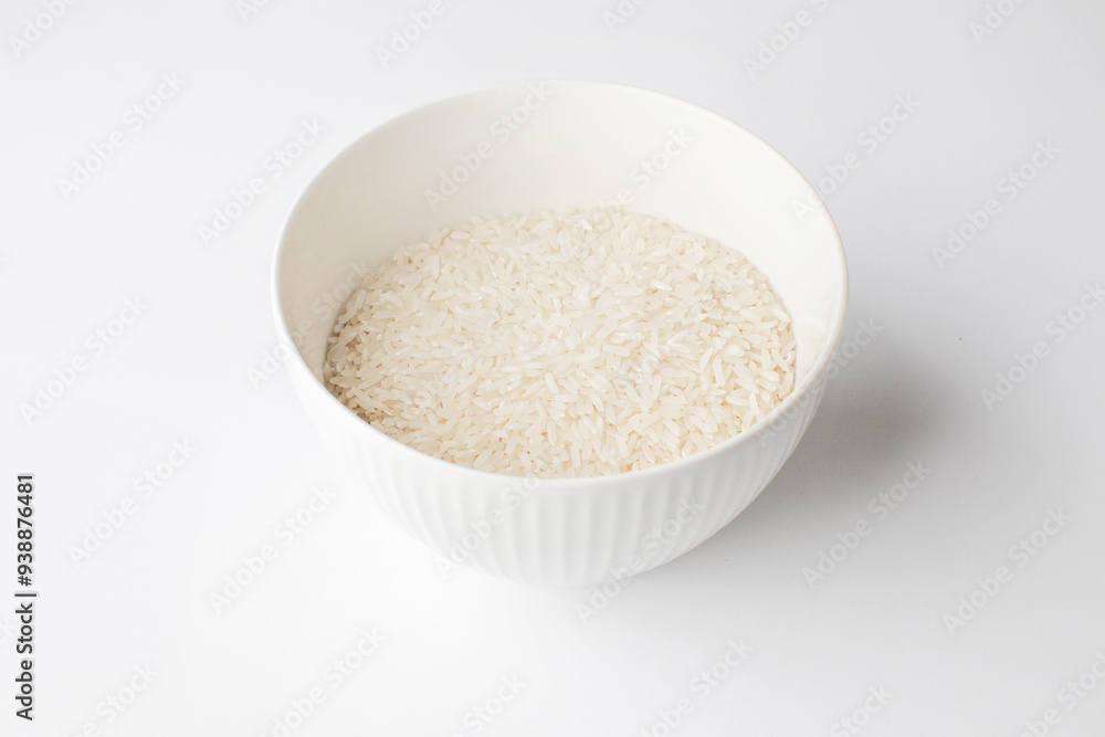 A ceramic bowl filled with uncooked white rice on a white background, optimal for illustrating concepts of basic nutrition or Asian cuisine preparation A ceramic bowl filled with uncooked white rice on a white background, optimal for illustrating concepts of basic nutrition or Asian cuisine preparation