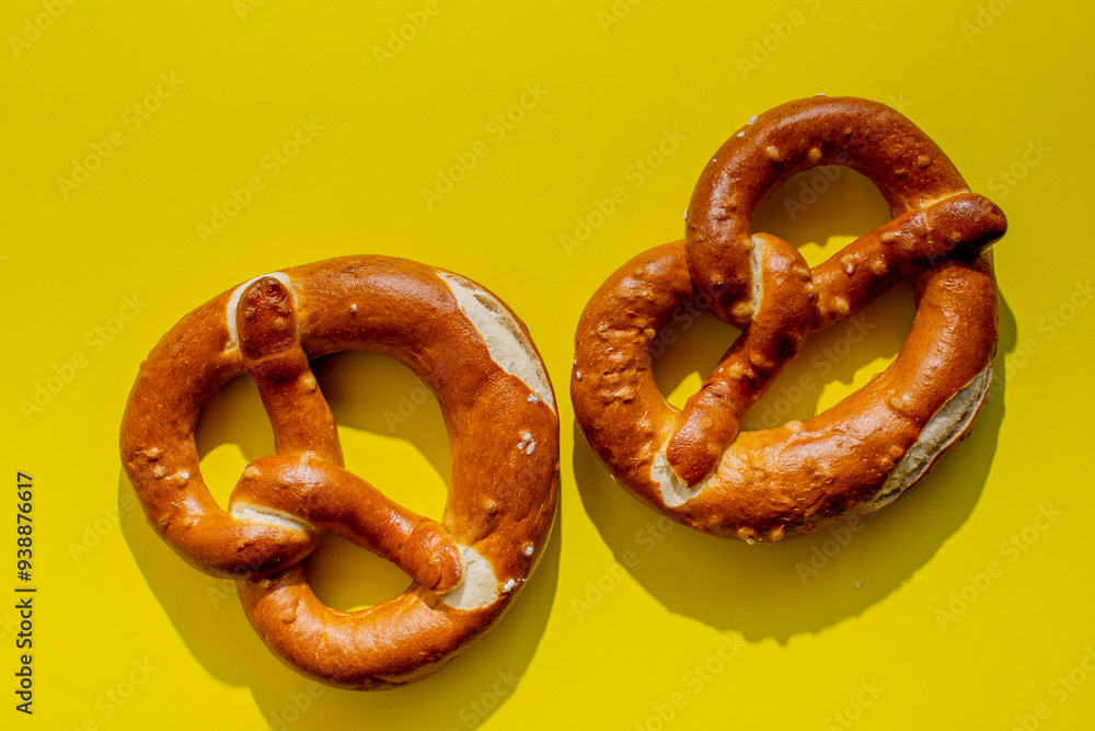 Two traditional German pretzels on a bright yellow background, perfect for Oktoberfest celebrations or bakery promotions