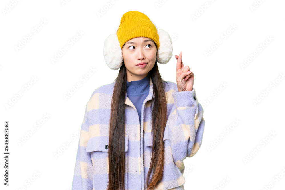 Young Asian woman wearing winter muffs over isolated chroma key background with fingers crossing and wishing the best Young Asian woman wearing winter muffs over isolated chroma key background with fingers crossing and wishing the best