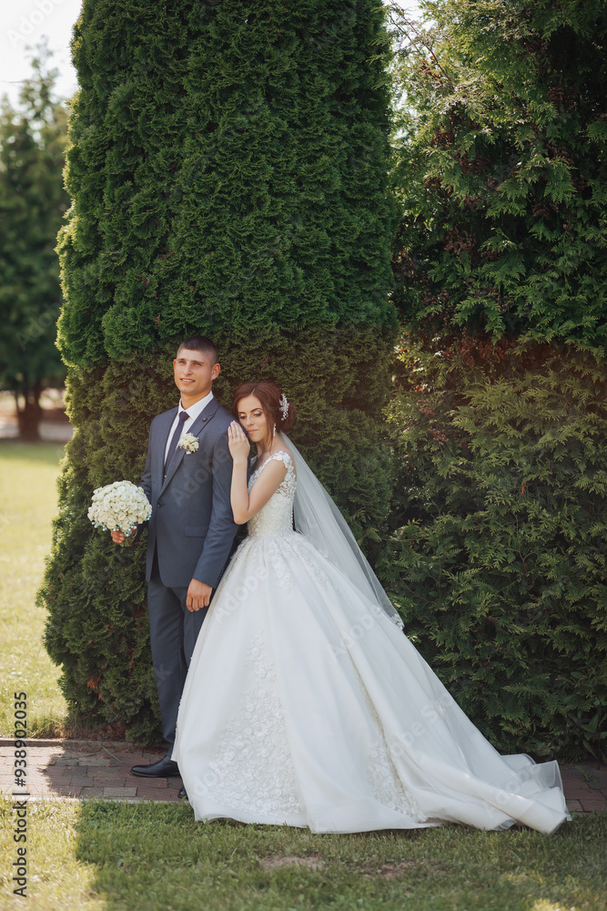 A bride and groom stand in front of a hedge, with the bride holding a bouquet. Concept of love and commitment, as the couple poses for a picture together. The green hedge adds a touch of nature A bride and groom stand in front of a hedge, with the bride holding a bouquet. Concept of love and commitment, as the couple poses for a picture together. The green hedge adds a touch of nature