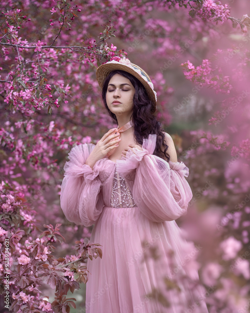 Portrait of a sensual girl in a lush pink dress among blooming apple trees