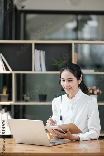 A woman is sitting at a desk with a laptop and a notebook