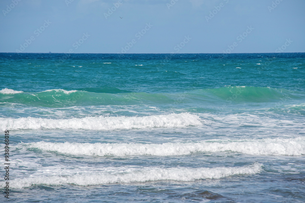 Waves Rolling Gently Onto Sunlit Shoreline With Clear Blue Water on Calm Day Waves Rolling Gently Onto Sunlit Shoreline With Clear Blue Water on Calm Day