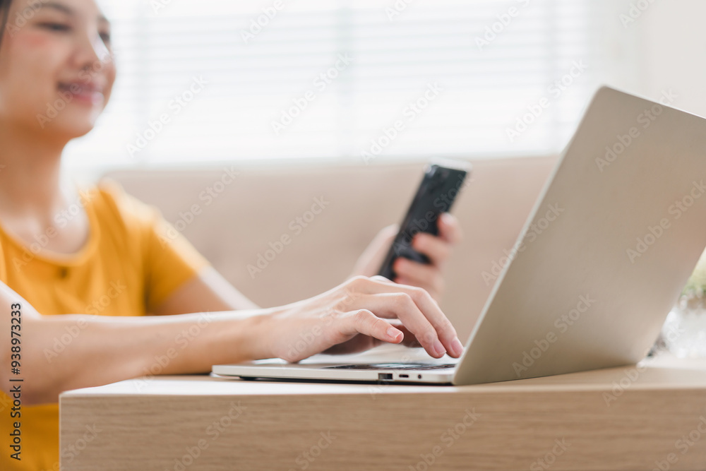 A woman in a yellow shirt works on her laptop while holding a smartphone, focusing on multitasking and staying connected. A woman in a yellow shirt works on her laptop while holding a smartphone, focusing on multitasking and staying connected.