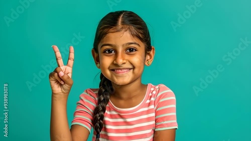 Young happy Indian girl sitting at a table and showing the ok sign with her hand isolated on a green background. photo