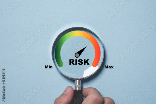 Hand holding magnifier glass with Risk level indicator rating since low to high on blue background for focus risk management and assessment concept. photo