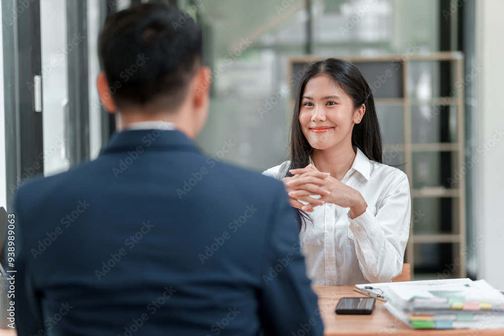 A man and a woman are sitting at a desk. The man is wearing a suit and the woman is wearing a white shirt. They are both smiling and seem to be having a pleasant conversation A man and a woman are sitting at a desk. The man is wearing a suit and the woman is wearing a white shirt. They are both smiling and seem to be having a pleasant conversation