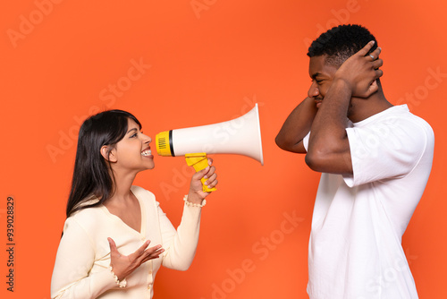 Woman Using Megaphone to Communicate With Man Covering His Ears Against an Orange Background